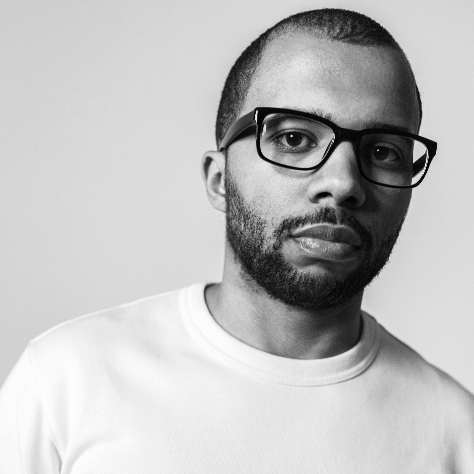 Close-up black and white portrait of a bearded man wearing glasses.
